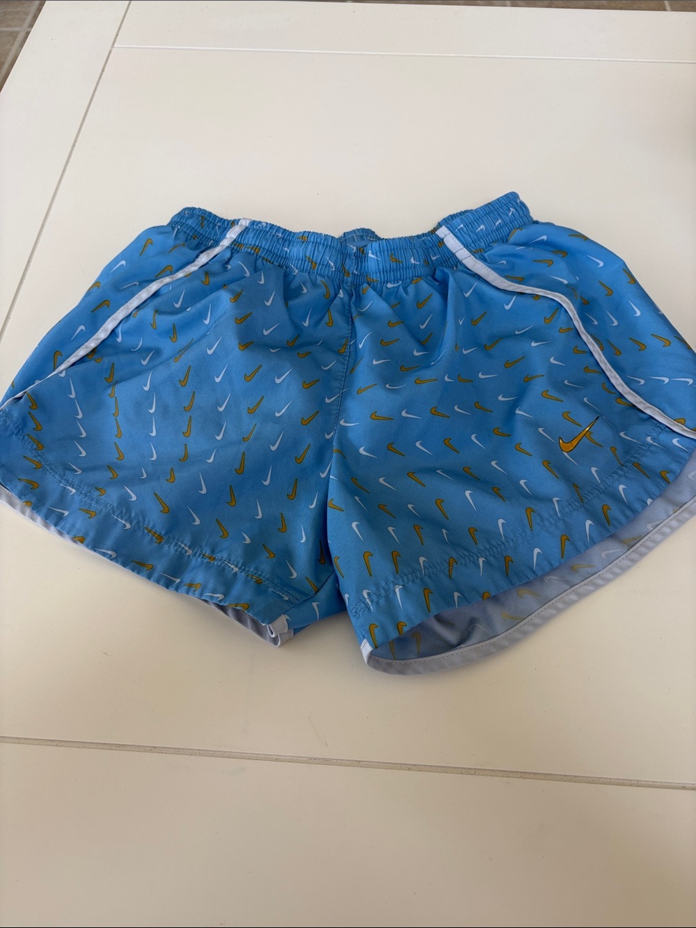 Nike Light Blue Girls Athletic Shorts with Gold Swoosh Pattern. Size M.